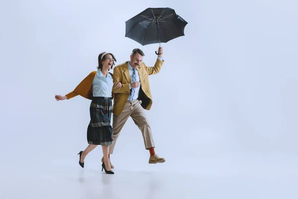 Unga glada familj par, man och kvinna i retro stil kläder, mode av 70-talet, 60-talet promenader med paraply isolerad på vit studio bakgrund — Stockfoto