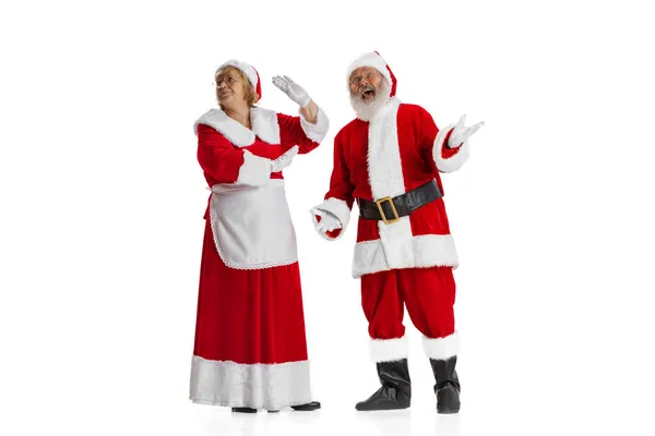 Excited senior man and beautiful woman, Santa Claus and missis Claus in traditional New Year costume isolated on white background. — Stock Photo, Image