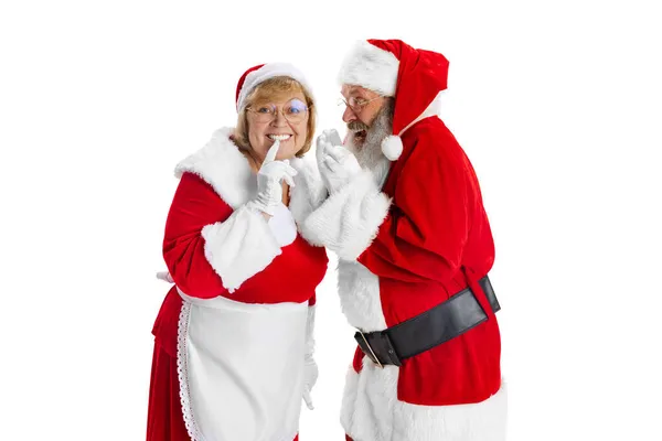 Gelukkig glimlachen oude man in Santa Claus kostuum en leuke vrouw, mevrouw Claus houden geheimen geïsoleerd op witte achtergrond. — Stockfoto
