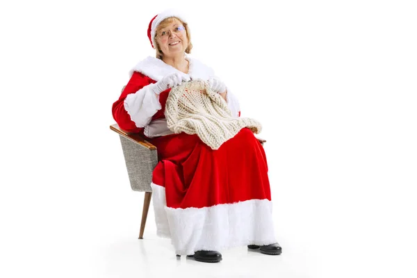 Portré boldog mosolygós gyönyörű középkorú nő karácsonyi jelmezben ül a karosszék és kötött pulóver elszigetelt fehér háttér. — Stock Fotó