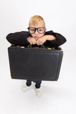 Yakından bakınca, yakışıklı küçük bir çocuk, büyük baba kıyafetli bir işadamı beyaz stüdyo arka planında izole edilmiş büyük klasik bir çanta tutuyor..