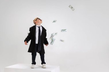 Duygusal küçük çocuk portresi, büyük ceket giymiş çocuk işadamı beyaz stüdyo arka planında izole edilmiş büyük bir kutunun üzerinde duruyor..