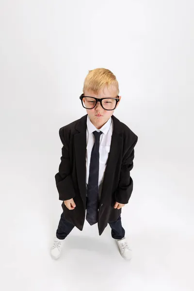 Високий кут зору милий маленький хлопчик, дитячий бізнесмен у величезній куртці в окулярах ізольований на білому фоні студії . — стокове фото