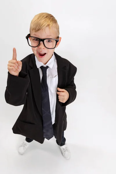 Hoge hoek uitzicht van emotionele kleine jongen, kind zakenman in enorme pak jas dragen bril geïsoleerd op witte studio achtergrond. — Stockfoto