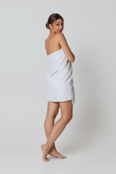 Portrét rozkošné mladé dívky v bílé koupeli ručník stojí sám izolovaný přes šedé pozadí studia. Přírodní krása, lázně, kosmetika — Stock fotografie