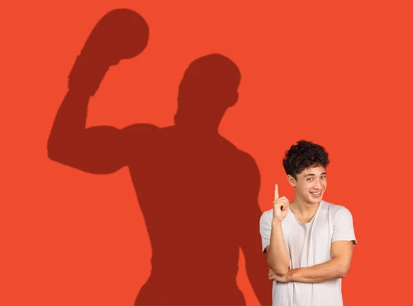 Un jeune homme qui pense à son avenir sportif. Image conceptuelle avec un garçon souriant et l'ombre du boxeur sur le mur rouge — Photo