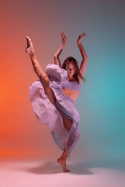 Dynamický portrét mladé ohebné soudobé tanečnice tanec izolované na gradient modré oranžové pozadí v neonu. — Stock fotografie
