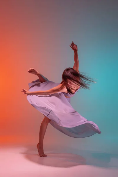Προσωπογραφία νεαρής ευέλικτης χορεύτριας που χορεύει απομονωμένη σε μπλε πορτοκαλί φόντο σε νέον. — Φωτογραφία Αρχείου