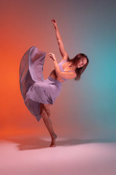 Porträtt av ung flexibel samtida dansare dans isolerad på lutning blå orange bakgrund i neon. — Stockfoto