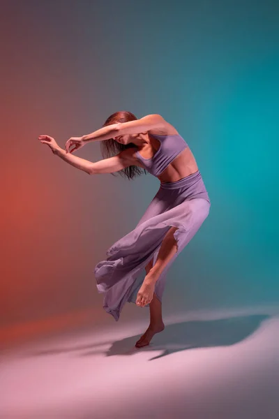Retrato de jovem dançarina de desprezo flexível na cor lilás palco traje dança isolado no gradiente azul laranja fundo em néon. — Fotografia de Stock
