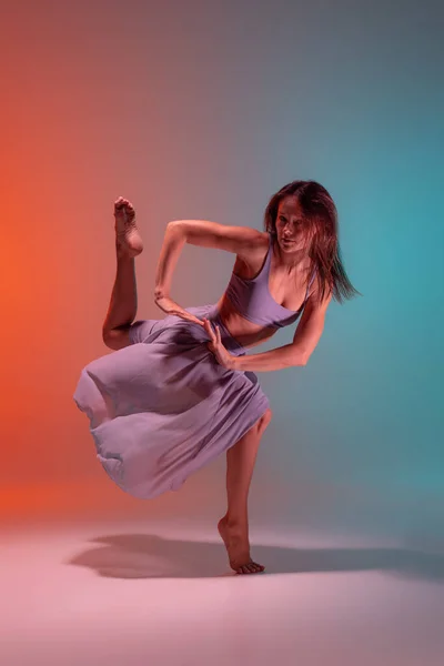 Porträtt av ung flexibel samtida dansare dans isolerad på lutning blå orange bakgrund i neon. — Stockfoto