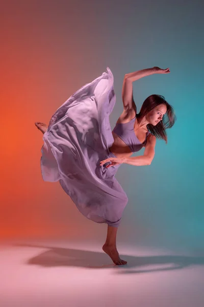 Retrato dinámico de la joven bailarina flexible de contemp bailando aislada sobre fondo azul anaranjado degradado en neón. — Foto de Stock