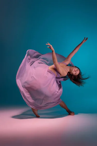 Um jovem dançarino de desprezo flexível em vestido lilás dançando isolado no gradiente azul fundo branco em néon. — Fotografia de Stock