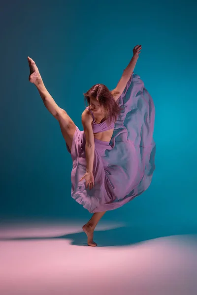Joven adorable bailarina flexible de contemp en vestido lila bailando aislada sobre fondo blanco degradado azul en neón. — Foto de Stock
