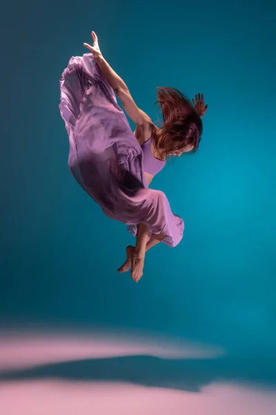 Joven adorable bailarina flexible de contemp en vestido lila bailando aislada sobre fondo blanco degradado azul en neón. — Foto de Stock