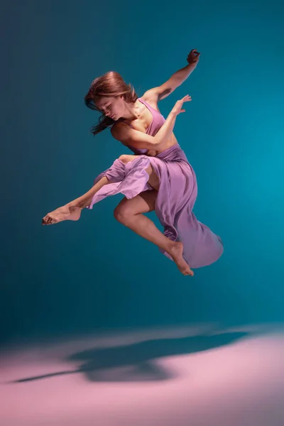 En ung flexibel samtida dansare i lila klänning dans isolerad på lutning blå vit bakgrund i neon. — Stockfoto