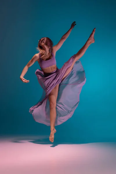 Jovem adorável dançarina de desprezo flexível em vestido lilás dançando isolado no gradiente azul fundo branco em néon. — Fotografia de Stock