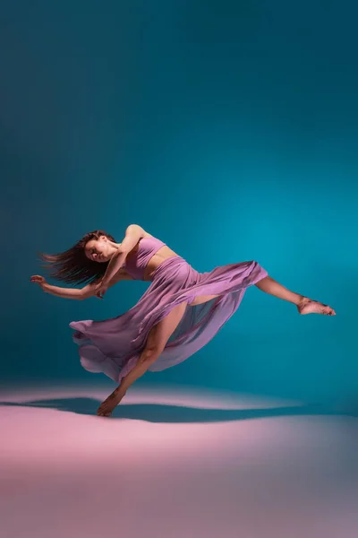 Una joven bailarina flexible de contemp en vestido lila bailando aislada sobre fondo azul degradado blanco en neón. —  Fotos de Stock