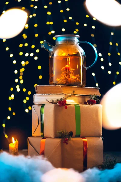 Magie nového roku. Čaj hrnec s teplým čajem stojící na dárkových krabicích přes tmavé pozadí s věnec světla. — Stock fotografie