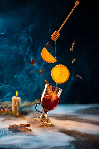 Design del biglietto di auguri. Tazza di vin brulè caldo con bastone di cannella e fette volanti di arance sulla tavola decorata di Natale. — Foto Stock