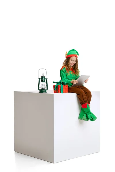 Linda chica sonriente vestida como gnomo divertido o elfo usando tableta, gadget aislado sobre fondo de estudio blanco. Invierno, vacaciones, concepto de Navidad —  Fotos de Stock