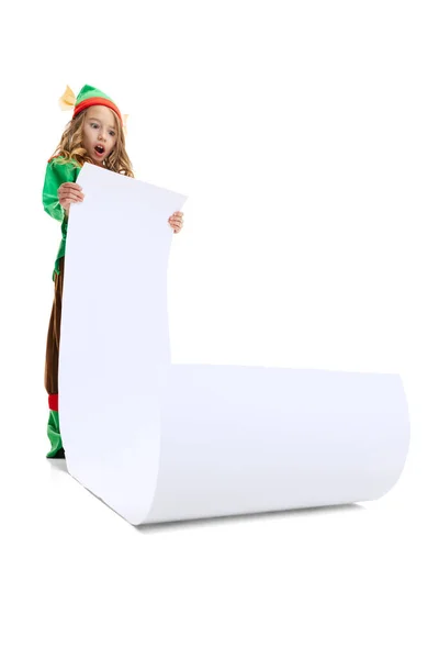 Маленькая смешная девочка, одетая как смешной гном или эльф с огромным бумажным листом, изолированным на белом фоне студии. Зима, праздник, рождественская концепция — стоковое фото