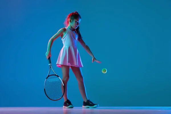 Одна маленька дівчинка, початківець тенісист позує ізольовано на синьому студійному фоні в неоновому світлі. Спорт, навчання, концепція дитинства — стокове фото