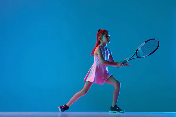 Retrato de niña, tenista principiante jugando al tenis aislado sobre fondo de estudio azul en luz de neón. Deporte, estudio, concepto infantil —  Fotos de Stock