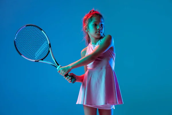 Jedna mała dziewczynka, początkująca tenisistka pozująca na niebieskim tle studia w neonowym świetle. Sport, nauka, koncepcja dzieciństwa — Zdjęcie stockowe