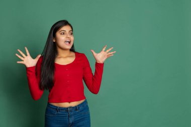 İhtişamlı genç, sevimli bir kız, günlük kıyafetleri içinde koyu yeşil stüdyo arka planında izole edilmiş poz veren bir öğrenci.