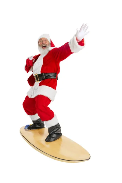 Portret emocjonalnego Mikołaja w czerwono-białym stroju stojąca deska surfingowa odizolowana na białym tle. Wesołych Świąt — Zdjęcie stockowe