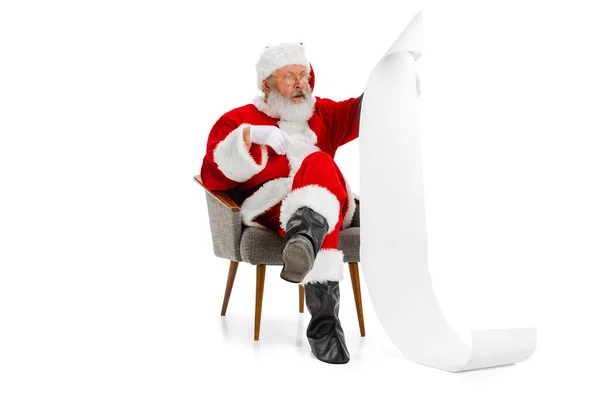 Portret van senior man, de Kerstman zittend op een fauteuil en wensenlijstje lezend, binnen. Gelukkig Nieuwjaar 2022, Kerstconcept — Stockfoto