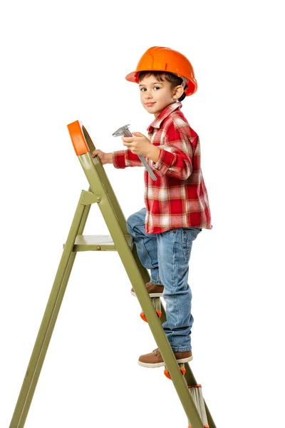 Portrait of little preschool boy, kid in image of builder, architect in orange protective helmet climbing ladder isolated on white background — Stock Photo, Image