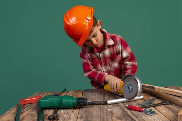 Portret uroczego chłopca, dziecko na zdjęciu budowniczego, projektant w pomarańczowym hełmie ochronnym przy użyciu narzędzi roboczych odizolowanych na zielonym tle — Zdjęcie stockowe