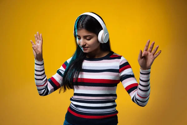 Emocional jovem bonito menina, estudante em roupas quentes ouvir música em fones de ouvido isolados na cor amarela estúdio fundo — Fotografia de Stock