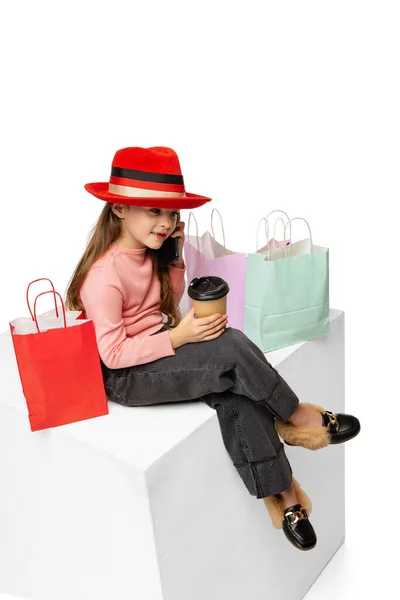 Портрет стильного симпатичного маленького ребенка в красной шляпе, сидящего на большой коробке на белом фоне. Красота, концепция моды — стоковое фото