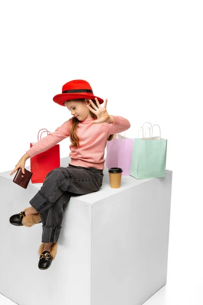 Porträt eines hübschen kleinen Jungen mit rotem Hut, der isoliert auf einer großen Box vor weißem Hintergrund sitzt. Schönheit, Modekonzept — Stockfoto