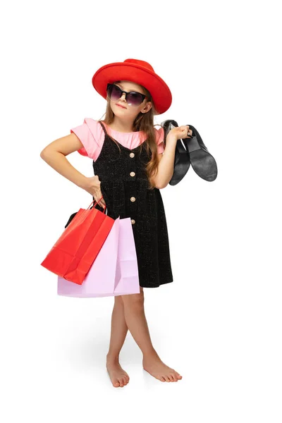 Стильная маленькая девочка, очаровательный ребенок, стоящий с разноцветными пакетами покупок и разговаривающий по телефону изолирован на белом фоне. — стоковое фото