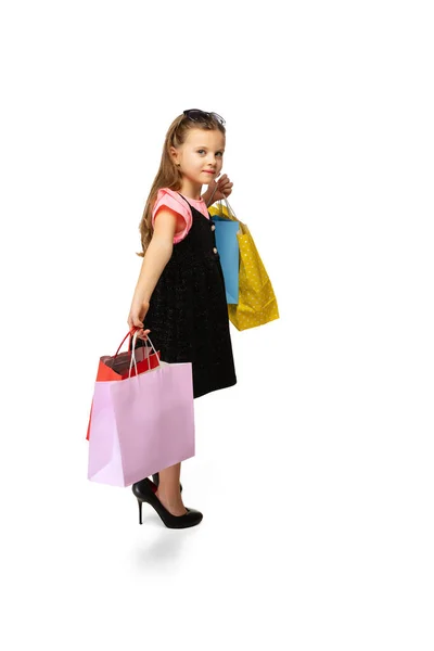 Студійний знімок досить маленької милої дитини, що стоїть з різнокольоровими пакетами покупок ізольовані на білому тлі . — стокове фото