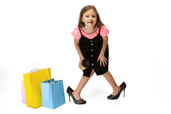 Концептуальный портрет симпатичного маленького симпатичного ребенка, стоящего с разноцветными пакетами покупок изолированы на белом фоне. — стоковое фото