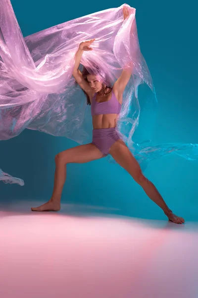Retrato dinâmico de jovem dançarina de desprezo flexível dançando com tecido isolado no gradiente azul fundo branco em luz de néon — Fotografia de Stock