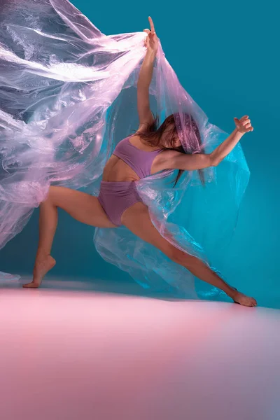 Δυναμικό πορτρέτο νεαρής ευέλικτης χορεύτριας που χορεύει με ύφασμα απομονωμένο σε μπλε φόντο σε νέον φως — Φωτογραφία Αρχείου