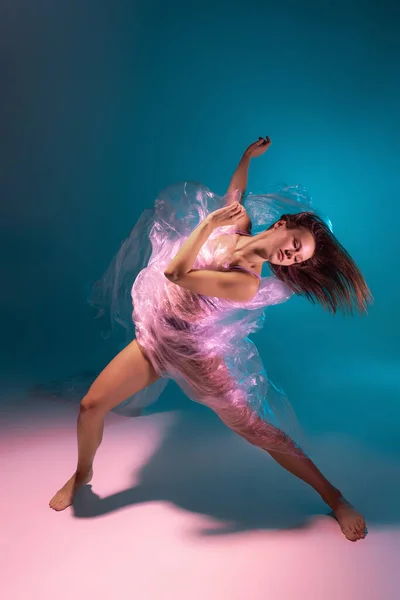 Сольное выступление. Красивая гибкая танцовщица танца с тканью, выделенной на градиентном синем фоне в неоновом свете — стоковое фото