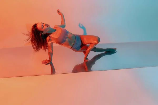 Giovane flessibile, ragazza aggraziata, ballerina accompagnatrice femminile in performance d'arte isolata su sfondo blu sfumato arancione al neon — Foto Stock