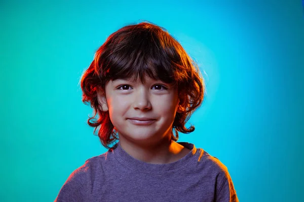 Félhosszú elülső fiúk portréja elszigetelve a kék stúdió hátterében neon fényben, szűrő. Emberi érzelmek, arckifejezés fogalma. — Stock Fotó