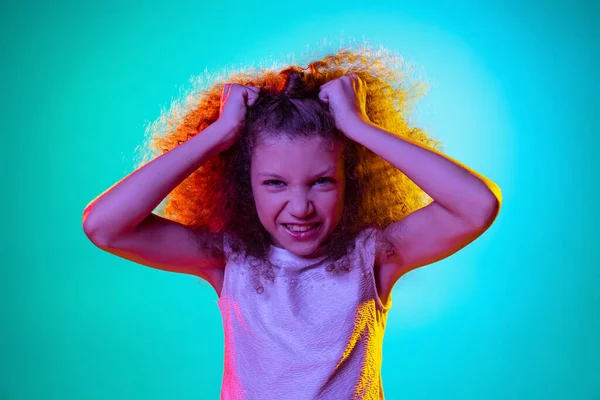Close-up kleine roodharige kind, walgelijk meisje kijken naar camera geïsoleerd op blauwe studio achtergrond in paars neon licht. — Stockfoto