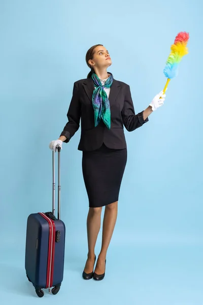 Estúdio tiro de menina bonita, comissário de bordo em uniforme com mala isolada no fundo do estúdio azul. — Fotografia de Stock