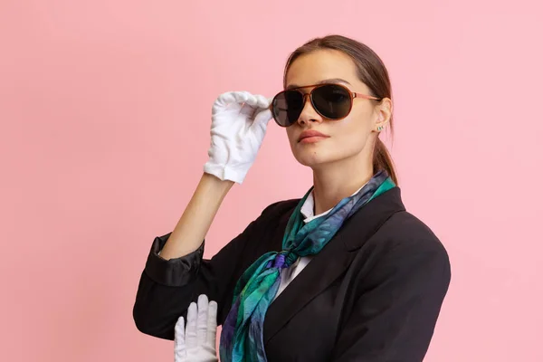 Stilvolles junges Mädchen, Flugbegleiterin mit Sonnenbrille blickt isoliert in die Kamera auf rosa Studiohintergrund. — Stockfoto