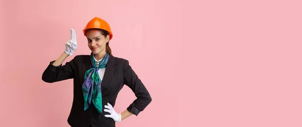 快乐的年轻姑娘，戴着橙色防护头盔的女乘务员，在粉红的摄影棚背景下显得孤立无援. — 图库照片