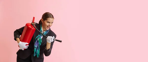 O Flyer. Menina feliz, assistente de bordo do sexo feminino com extintor de incêndio se divertindo isolado no fundo do estúdio rosa. — Fotografia de Stock